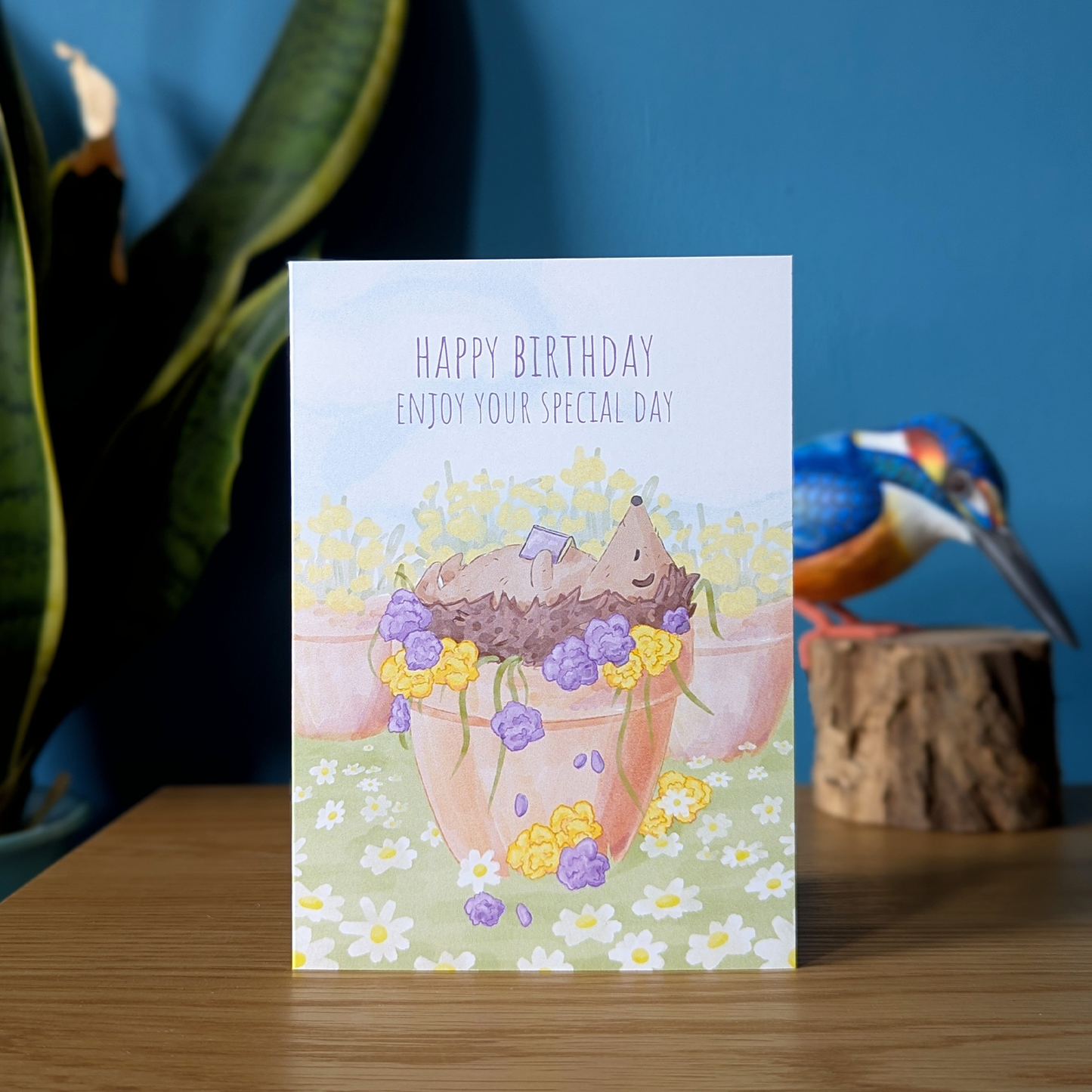 happy birthday hedgehog card for book lovers. This card features a hedgehog sleeping in a plant pot of flowers, under the sun with a book on her lap