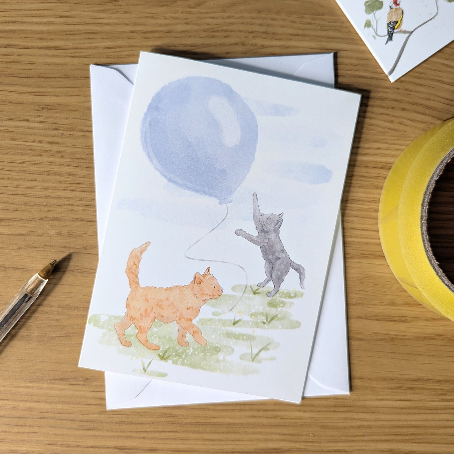 A cute kitten birthday card with a grey and ginger cat chasing a blue balloon