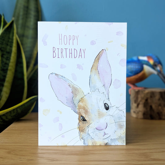 "Hoppy Birthday" - Rabbit birthday Card featuring a white, grey and brown bunny rabbit hopping out of the corner of the card