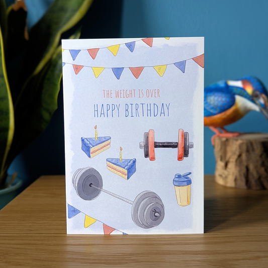 gym birthday card for men with the message 'the weight is over'. The card has birthday cake, dumbbell, barbell, protein shake illustrations